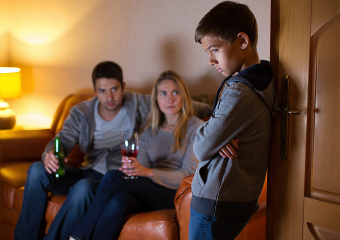 Подросток наблюдает за тем, как родители пьют алкоголь дома, демонстрируя влияние семьи